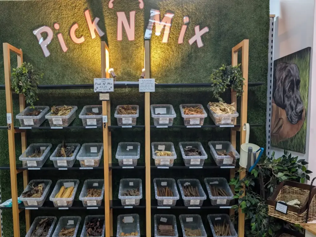 Pick N Mix wall at Ace K9 Doggy Deli, with tubs of natural dog treats on wooden shelves against a grass wall